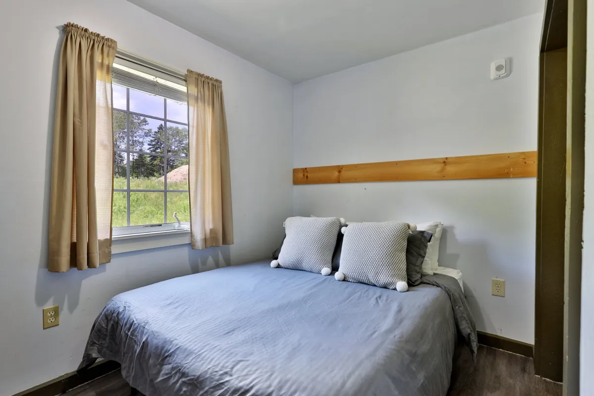 A serene bedroom featuring a comfortable bed with decorative pillows, a wooden wall accent, and natural light streaming through the window. The space is designed for rest and relaxation, with inviting textures and a cozy atmosphere.