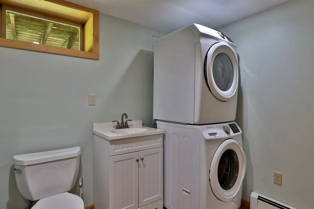 A functional laundry area with a stacked washer and dryer, a compact sink and cabinet, and a small window providing natural light. The setup is practical and essential for longer stays.