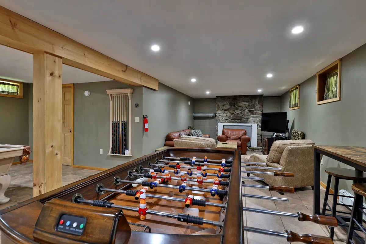 A spacious social area with a foosball table, stone fireplace, leather sofas, and bar stools. The room is filled with natural light and blends relaxation with lively activity, making it ideal for group gatherings and hosting game nights.