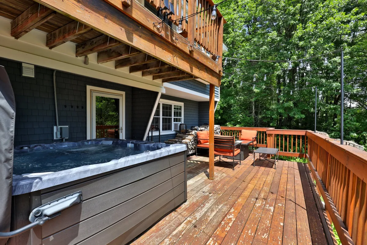 An inviting scene featuring a bubbling hot tub on a wooden deck, surrounded by lush foliage. The area includes comfortable deck seating, perfect for both relaxing and entertaining, and seamlessly blends into the natural yard beyond.