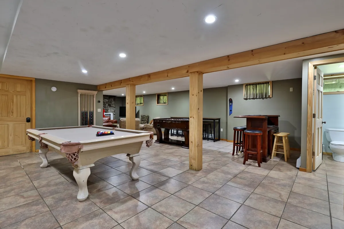 A stylish game area featuring a pool table and a bar area, surrounded by comfortable seating. The space is designed for friendly competition, casual drinks, and group fun, with an open feel that connects it to other living areas.