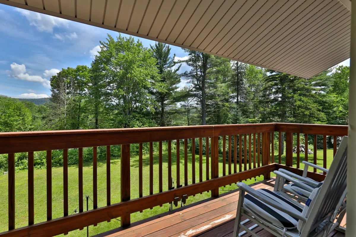 A peaceful shot from the wooden deck, overlooking a spacious lawn and lush green trees. The image captures the sense of openness and tranquility that comes with being surrounded by nature.