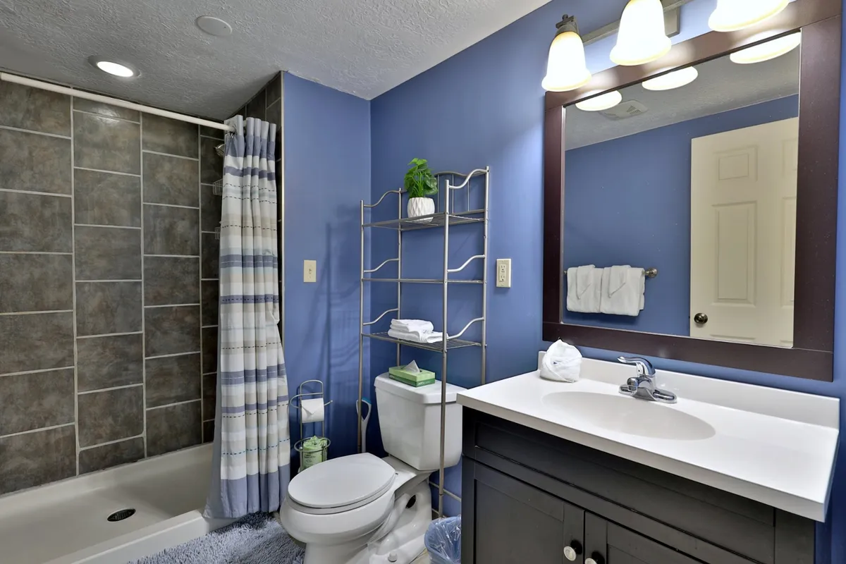A modern bathroom featuring a spacious shower area, a mirrored vanity, and open shelving for towels and essentials. The space feels refreshing and serene, ideal for morning and evening routines.