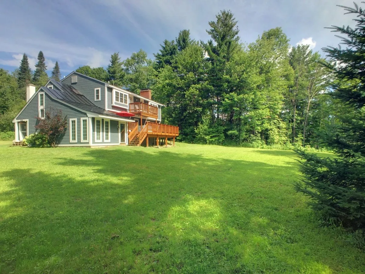 A tranquil view of the house set among trees, highlighting the deck area and a private yard ideal for children playing and adults enjoying shade or a barbecue. The image evokes a sense of peace and room for everyone to spread out.