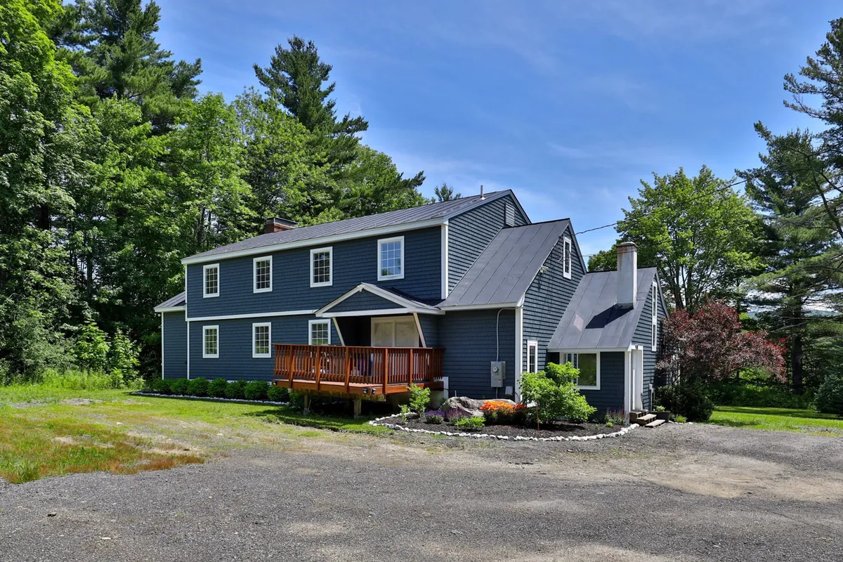 This image shows the blue exterior of the Bigelow Chalet, with its spacious wooden deck and lush greenery surrounding the property. The deck is an inviting spot for outdoor gatherings and relaxation, seamlessly connecting the home to the natural landscape.