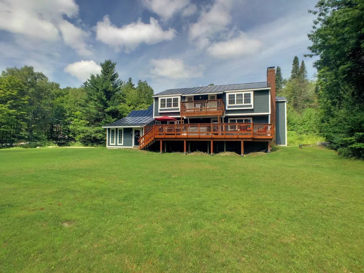 An expansive wooden deck bordered by lush trees and a green lawn, featuring ample space for outdoor dining and relaxation. The setup is perfect for barbecues, sunset dinners, or enjoying morning coffee in the fresh mountain air.