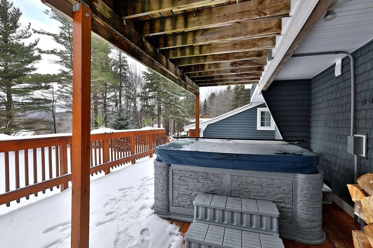 A bubbling hot tub sits on the wooden deck, surrounded by snow and trees. The snowy backdrop and inviting warmth of the hot tub suggest relaxation after a day of productive meetings or team activities, highlighting one of the property’s most attractive amenities for unwinding with colleagues.